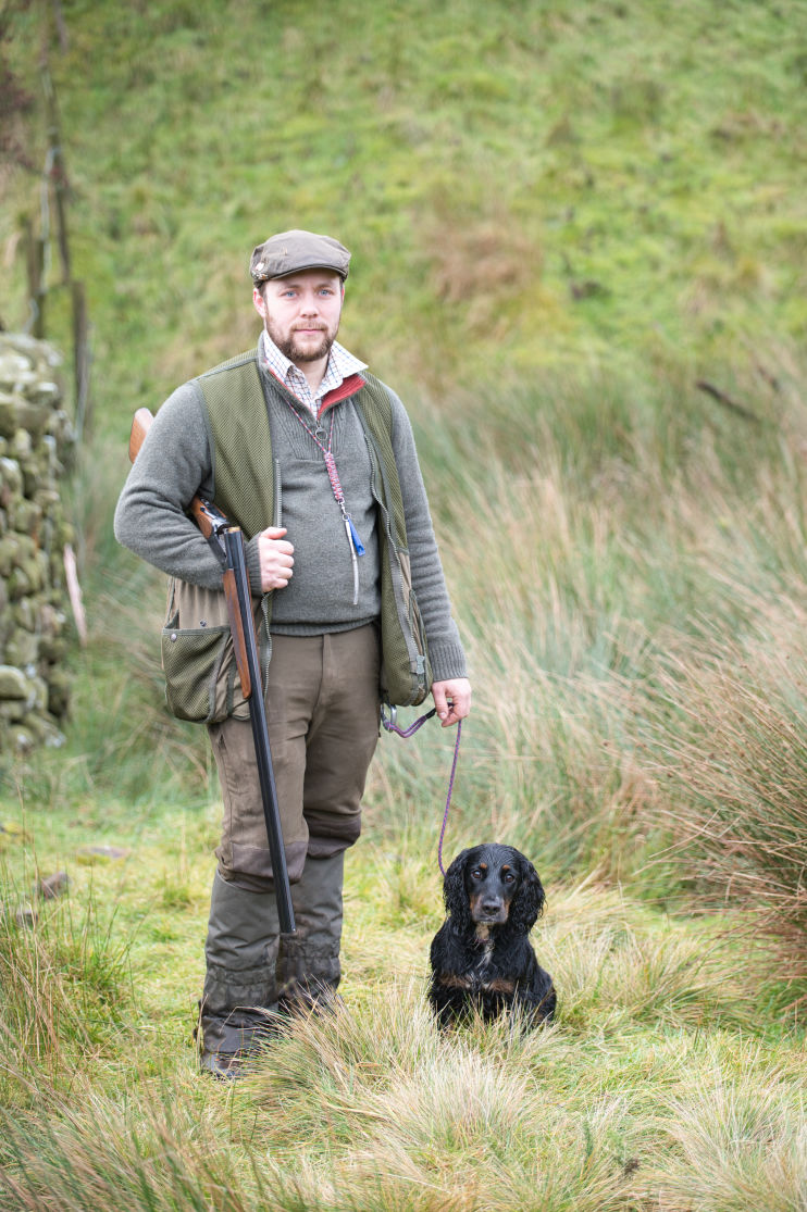 Man standing at his peg with his young cocker spaniel, waiting for the drive to begin. 